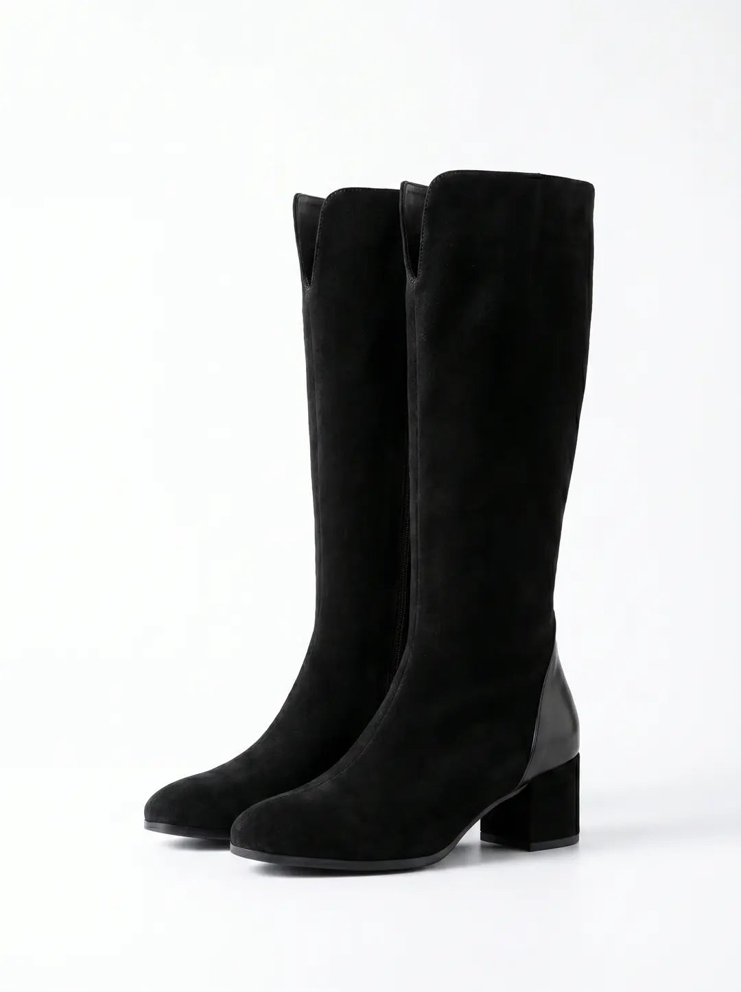 Dos botas altas negras de gamuza con detalles de cuero liso en el talón y tacón de bloque, sobre un fondo blanco.