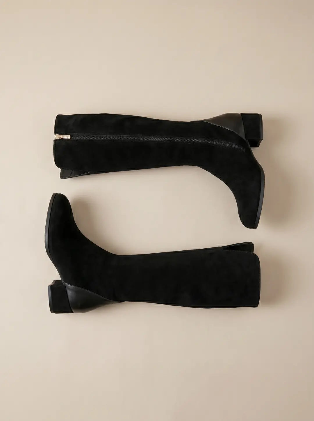 Dos botas negras de caña alta de ante. Una de las botas tiene una cremallera lateral visible. Ambas presentan un tacón bajo y cuadrado.