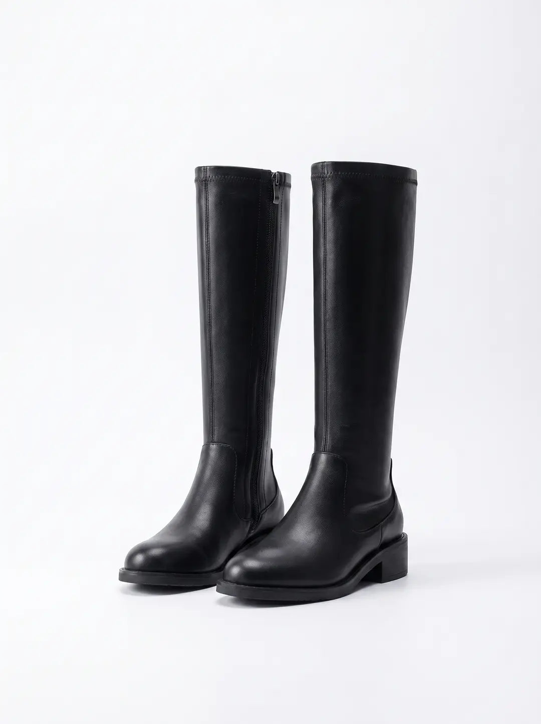 Un par de botas altas negras de cuero liso con tacón bajo. La bota izquierda tiene una cremallera lateral.