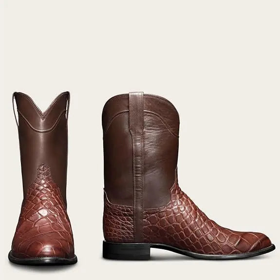 Par de botas vaqueras marrones. Una bota se ve de frente y la otra de perfil. La parte inferior tiene una textura de piel de cocodrilo o caimán marrón, y la parte superior es de cuero liso marrón. Las suelas son negras.