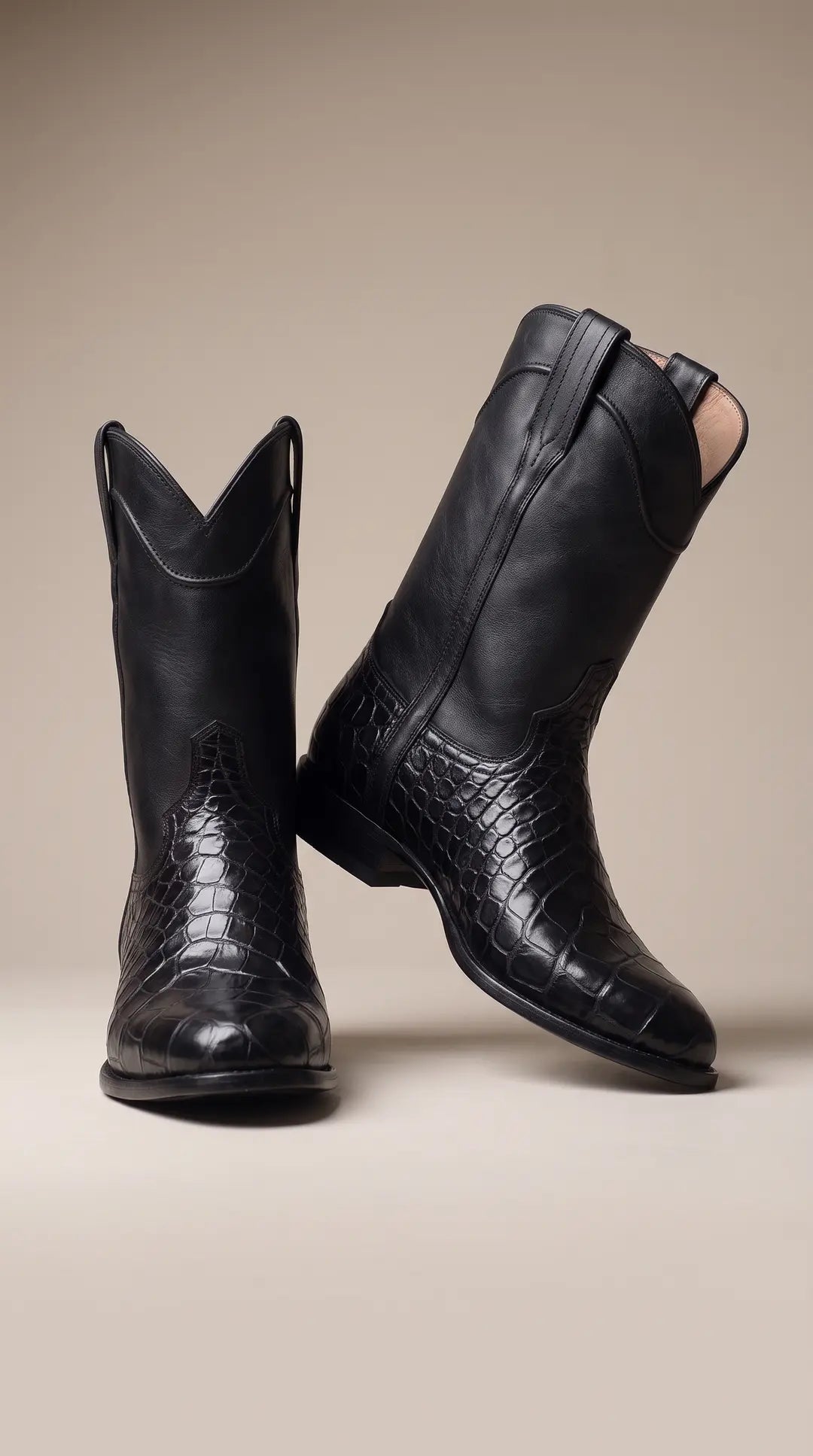 Par de botas de estilo vaquero negras. Una bota está de pie mirando hacia adelante y la otra está inclinada con el tacón elevado, mostrando el perfil. Ambas botas tienen piel texturizada de cocodrilo en la parte inferior y piel lisa en la caña superior.