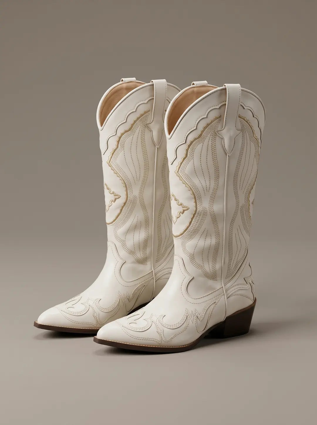 Par de botas vaqueras blancas con puntera puntiaguda y tacón marrón oscuro. Presentan costuras decorativas intrincadas en tono beige que adornan la caña y el empeine.