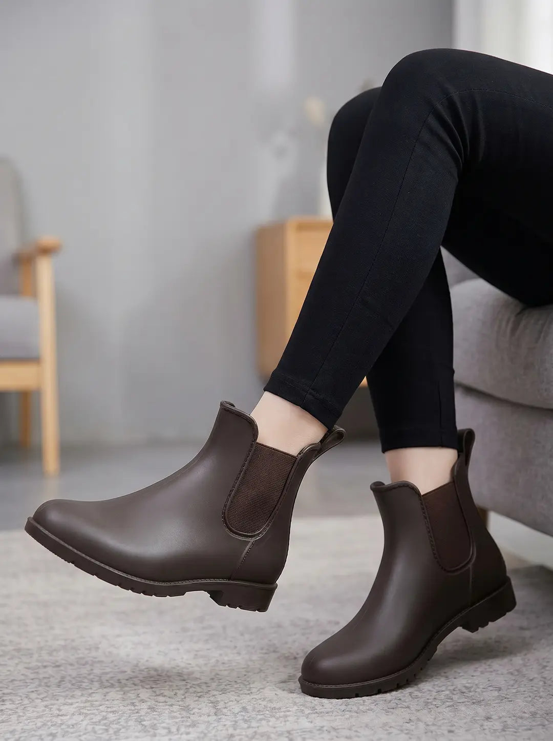 Un par de botines estilo Chelsea de color marrón oscuro con paneles elásticos laterales y suela texturizada, siendo usados con pantalones negros.