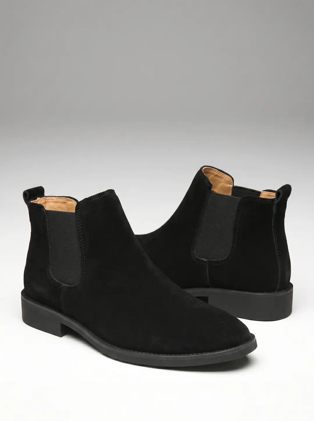 Par de botas Chelsea negras de ante con paneles el
r
el
sticos laterales y suelas planas negras. El forro interior visible es de color beige claro.