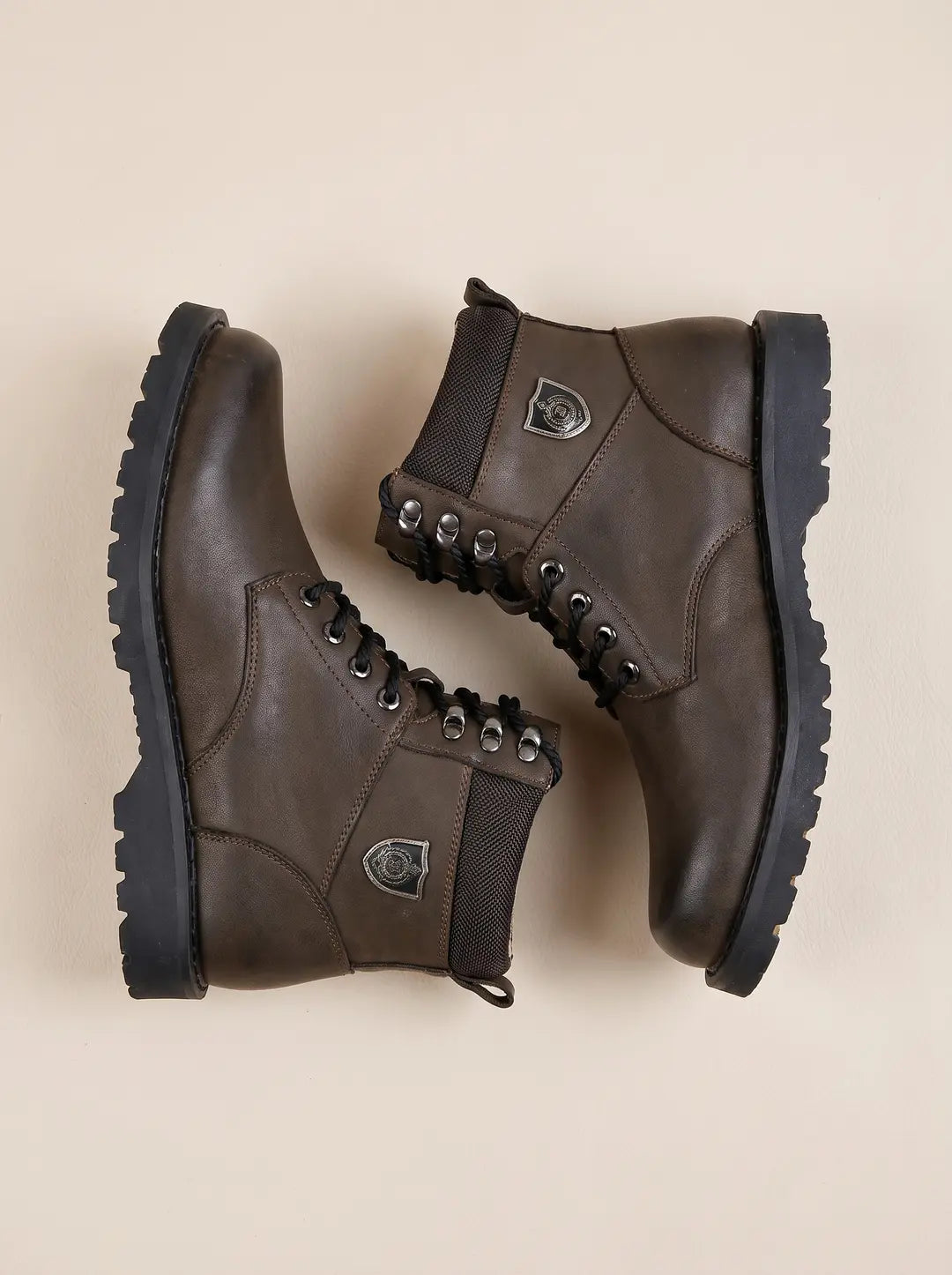 Par de botas marrones con cordones negros y suelas negras gruesas sobre una superficie clara.