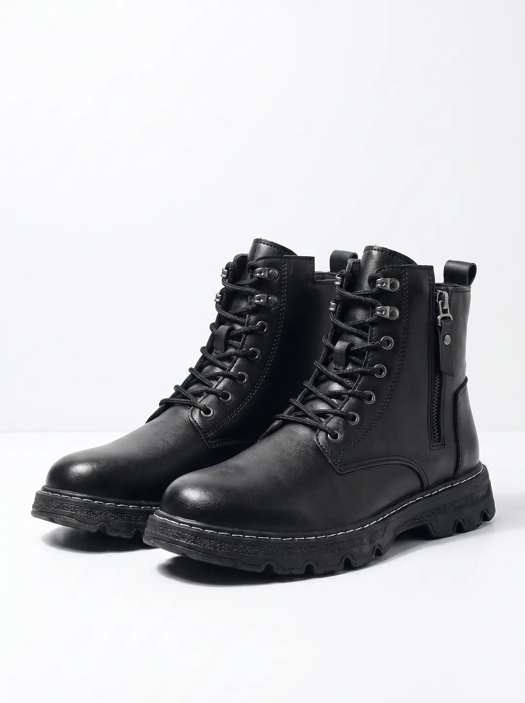Par de botas negras de cuero sintético con cordones, suela gruesa y costuras blancas en contraste. Una de las botas tiene una cremallera lateral visible. El fondo es blanco.