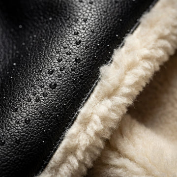 Detalle macro de cuero negro resistente al agua con gotas de lluvia y forro térmico interior de chiporro blanco. Tecnología de invierno Tierra Ruda.