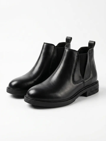 Un par de botines Chelsea negros de cuero con paneles laterales elásticos, tiradores traseros y suelas negras. La palabra 'fashion' está grabada en el tacón de la bota derecha.