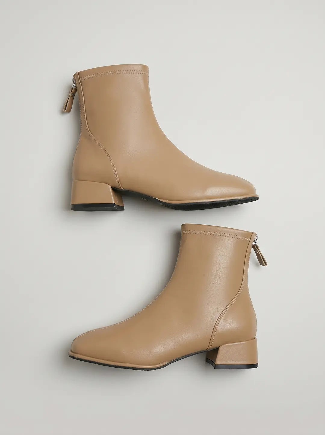 Dos botines de color beige claro, con cremallera en la parte trasera y tacón bajo de bloque.