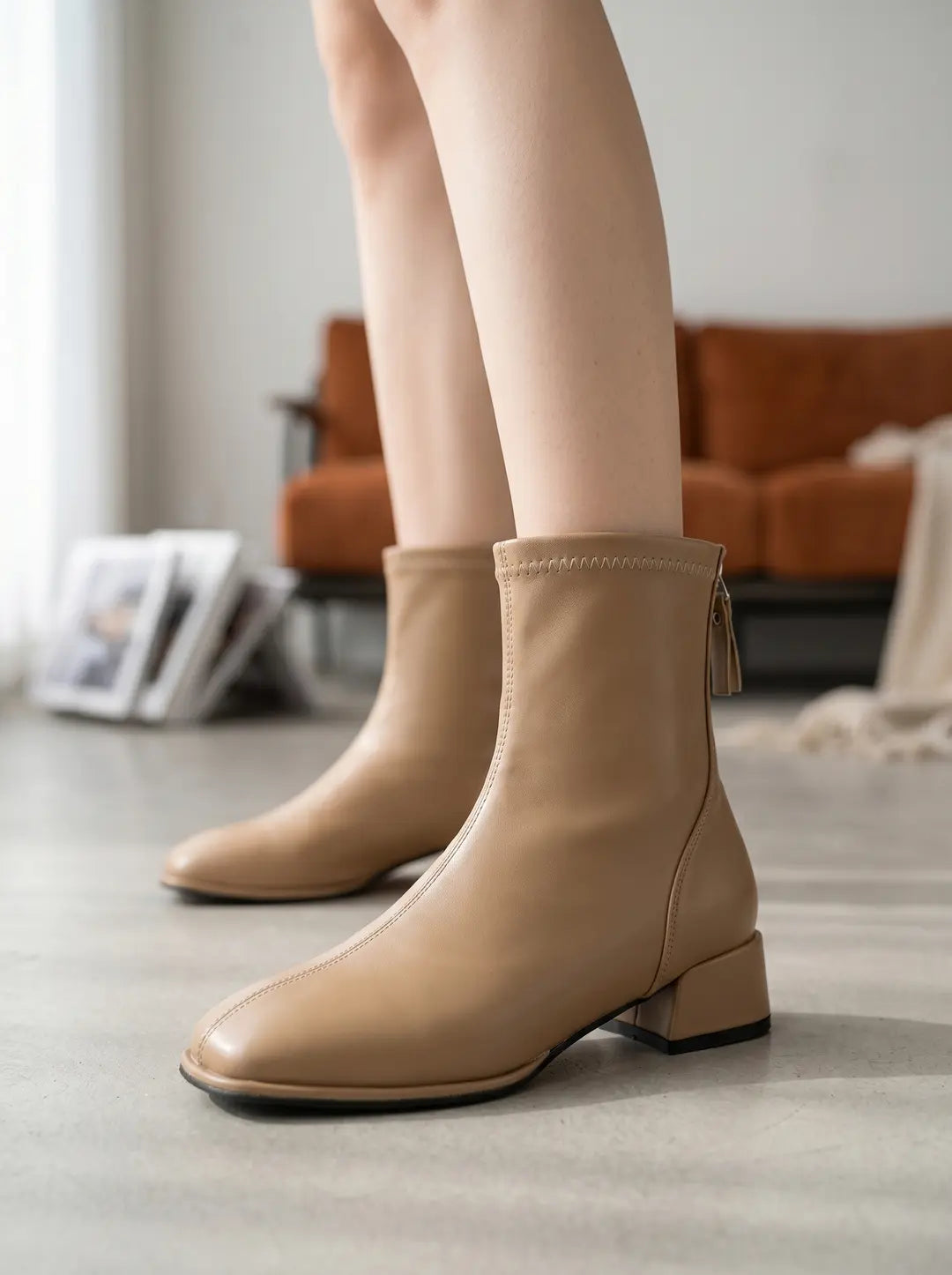 Par de botines de color beige claro con punta cuadrada y tacón bajo. Cuentan con una cremallera trasera y costuras visibles.