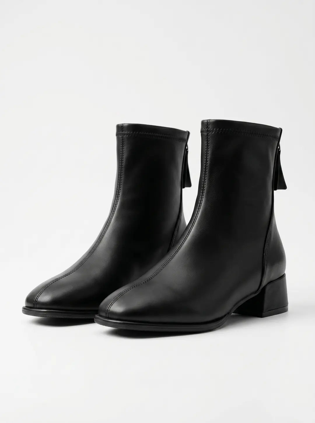 Par de botines negros de tacón bajo con cremallera trasera y una costura vertical frontal, sobre un fondo blanco.