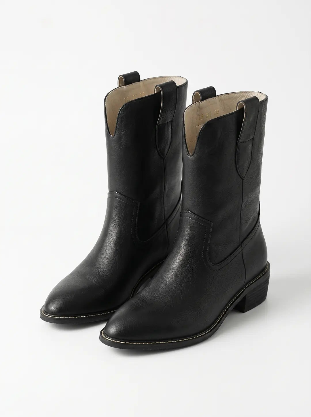 Un par de botas de estilo vaquero negras con superficie texturizada, puntera puntiaguda, tacón de bloque y costuras decorativas visibles.