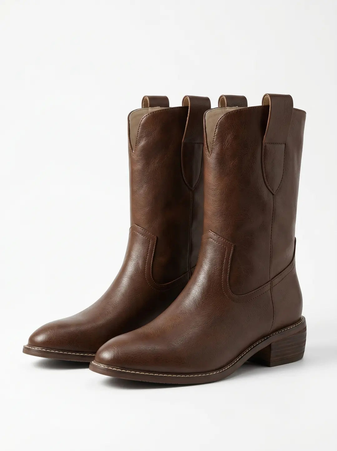 Par de botas vaqueras marrones con textura, punta puntiaguda, tacón apilado y detalles de costura, sobre un fondo blanco.