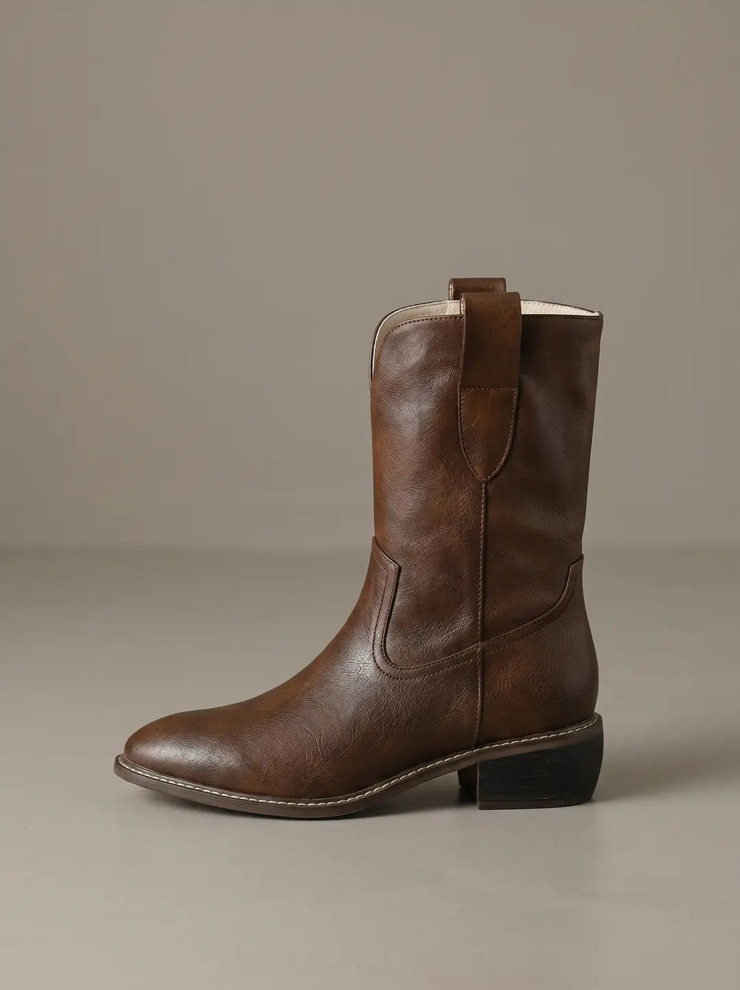 Bota vaquera marrón con tacón bajo y costuras decorativas visibles en el lateral y la suela.